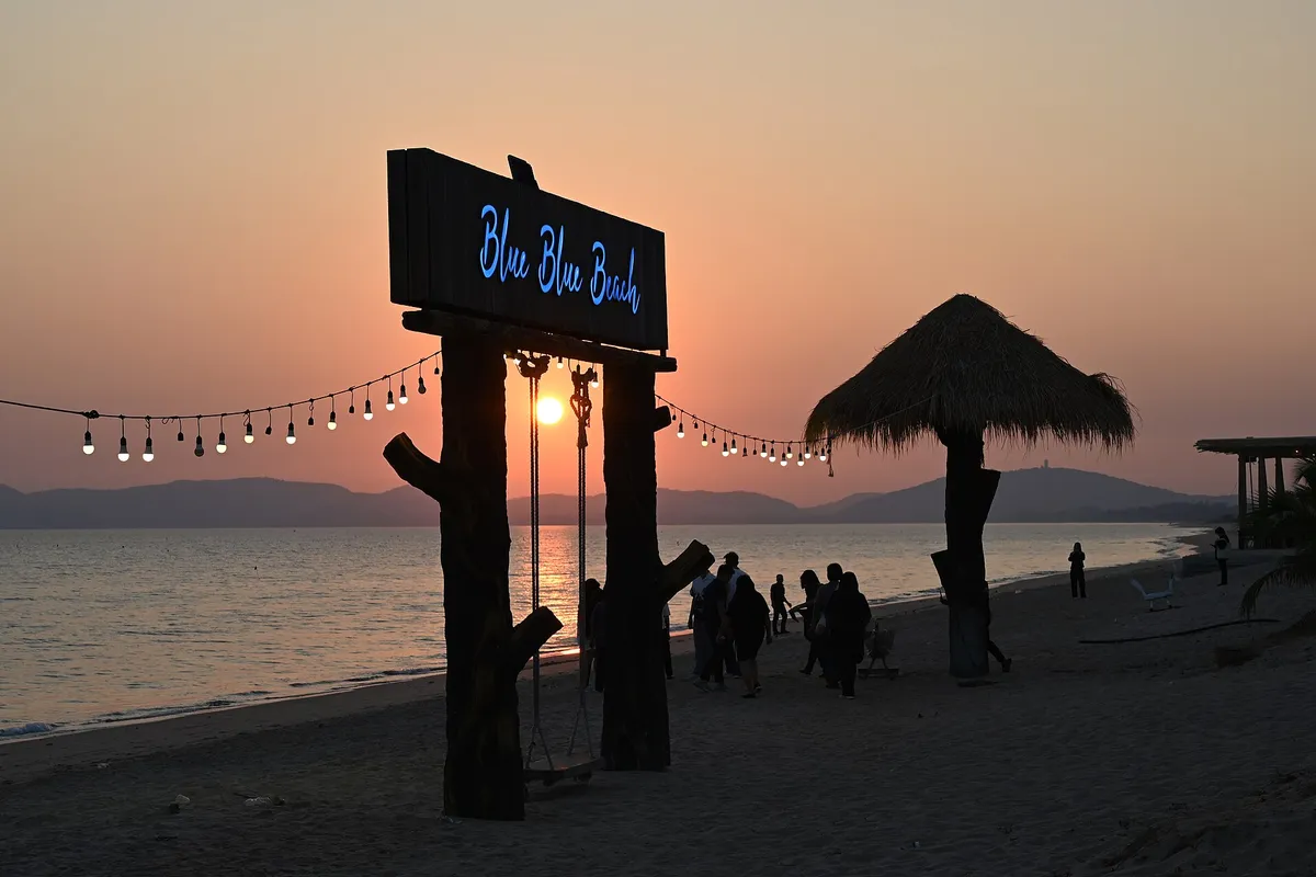 DZ6 2674 Blue Blue Beach - golden hour on the shoreline where string lights and palm-thatched huts welcome sunset strollers
